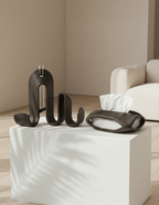 AMINI STRIA Entry Set in Charcoal — book holder and tissue holder on a white cube pedestal in a neutral living room