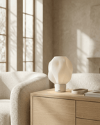 AMINI STRIA Lamp in White — lit on a wooden sideboard in a warm living room with boucle armchairs and leaf shadows