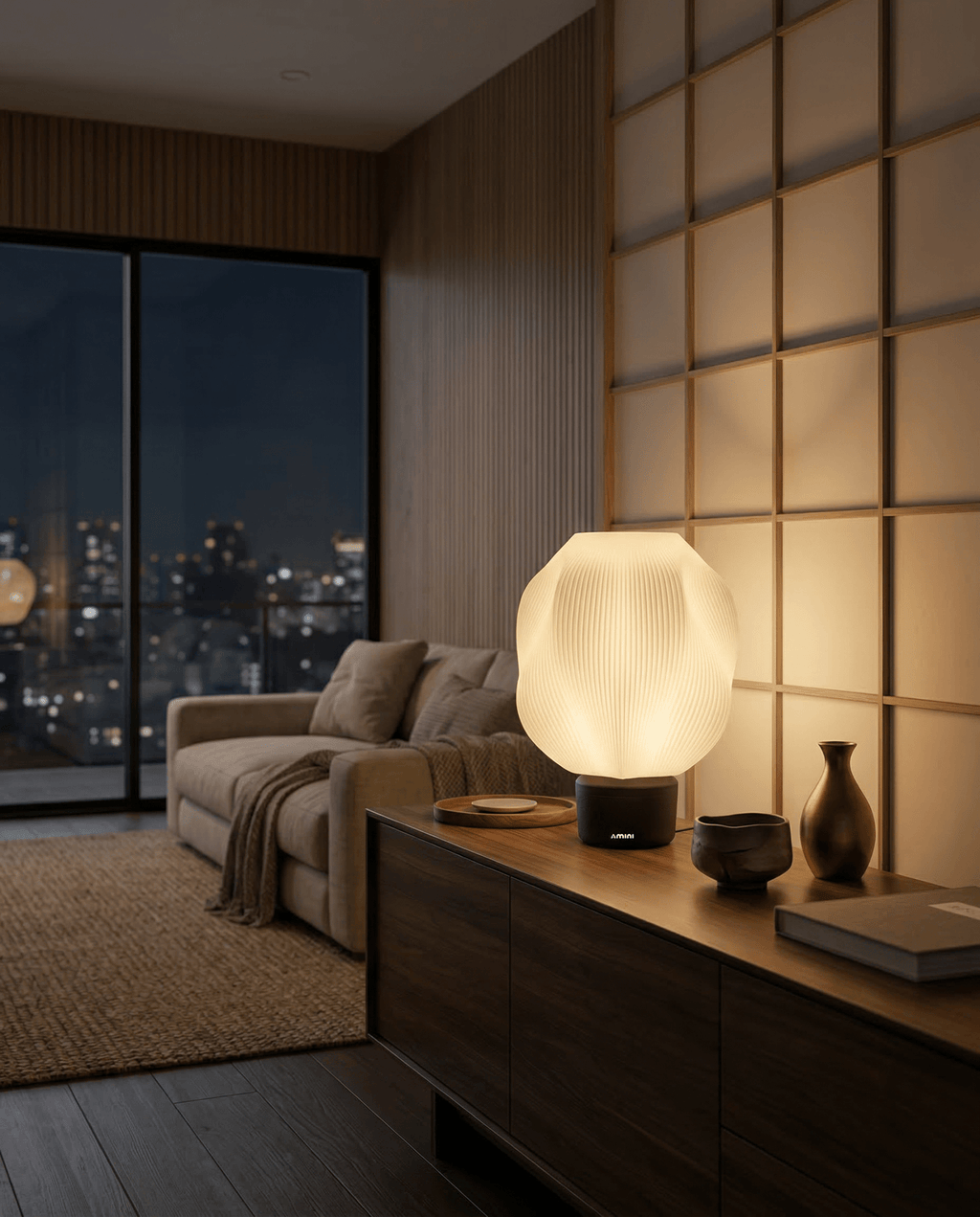 AMINI STRIA Lamp in Charcoal — lit at night on a sideboard in a Japanese-style room with warm glow and city skyline