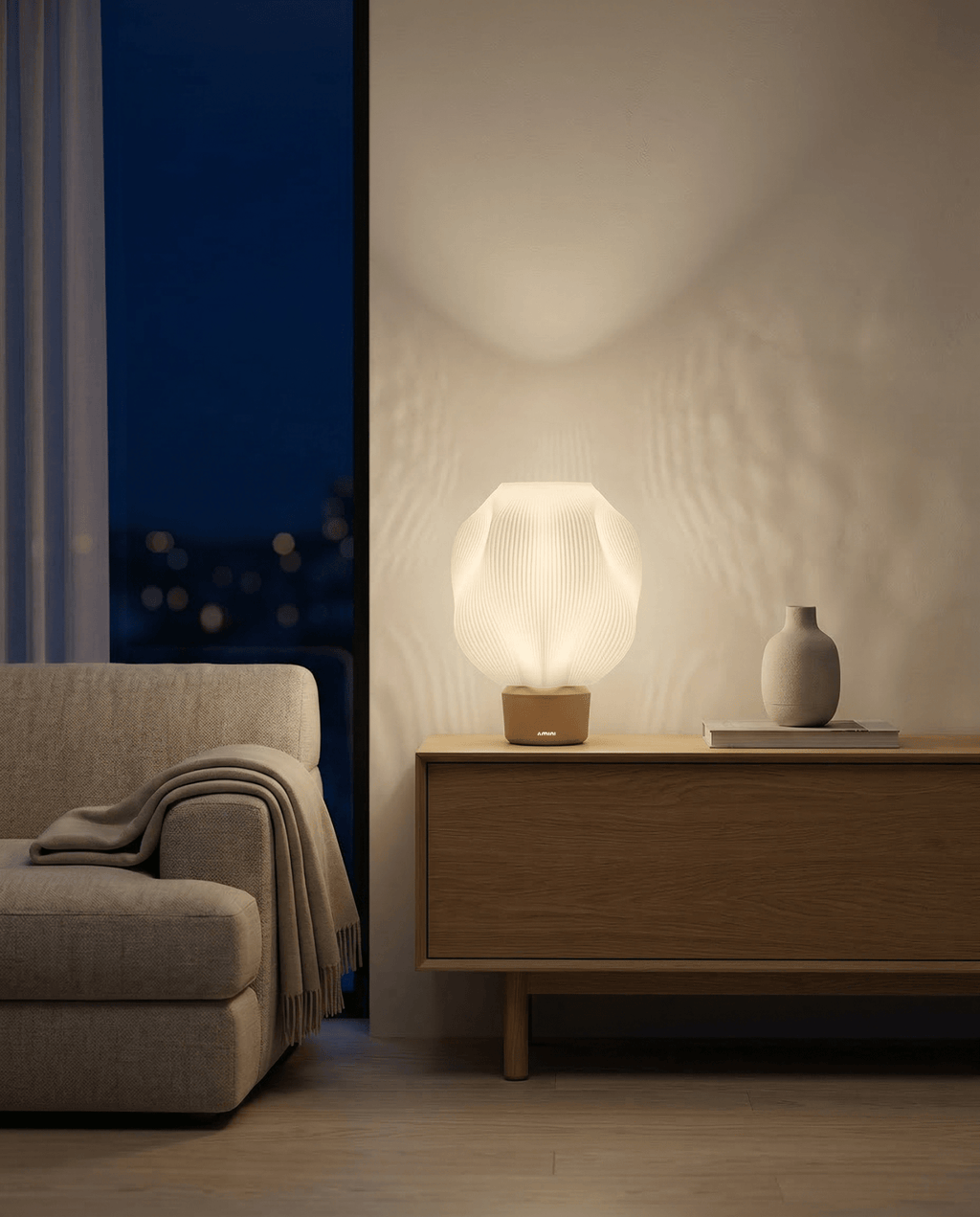 AMINI STRIA Lamp in Cream — lit at night casting warm light shadow on wall, city lights through curtained window