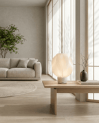 AMINI STRIA Lamp in White — on a low coffee table in a bright Scandinavian-style living room with dark vase and branches
