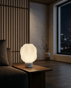 AMINI STRIA Lamp in White — lit at night on a side table against a wood slat wall, city lights through window